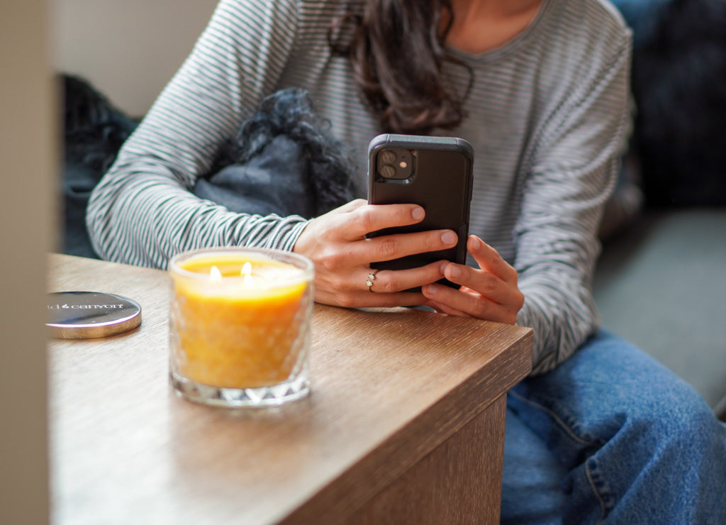 Person using phone pictured next to Gold Canyon's Fresh Orange candle. 