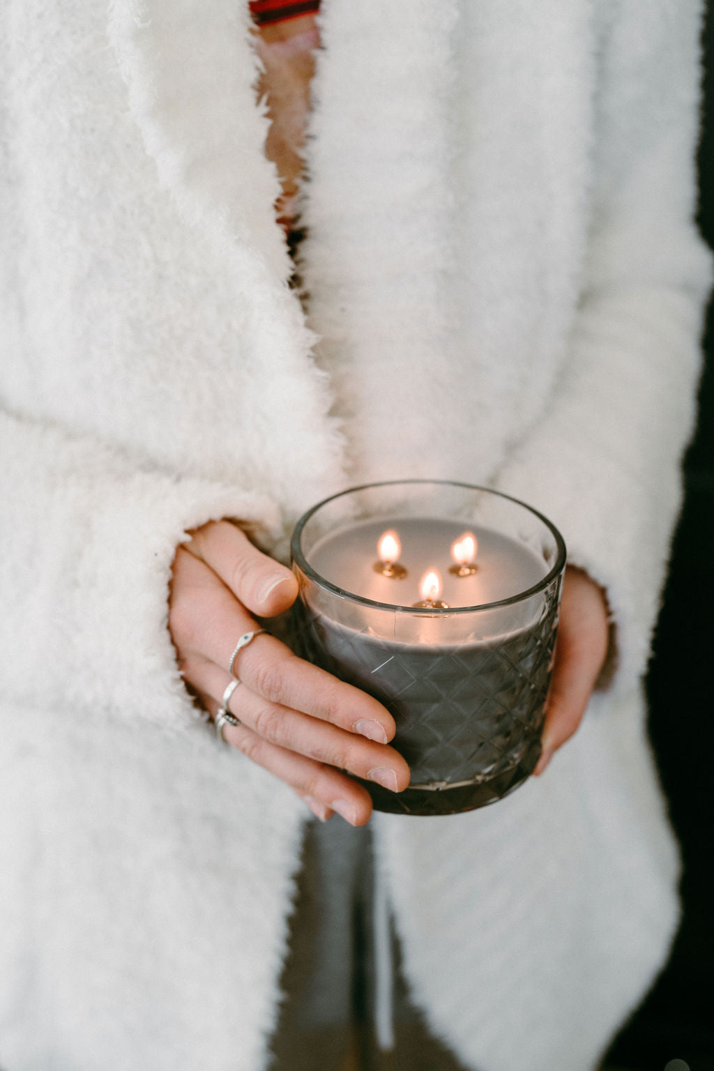 Driftwood candle held with two hands and white fluffy robe.